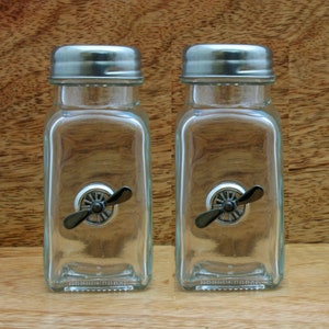 May include: Two clear glass salt and pepper shakers with silver lids and a propeller design on the front.