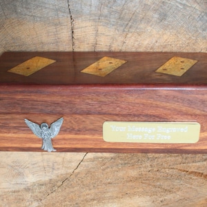 May include: A wooden box with a hinged lid, featuring three inlaid dominoes with gold-colored dots. The box has a silver angel figurine on the front and a brass plaque that reads "Your Message Engraved Here For Free".