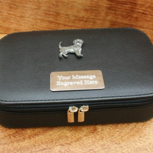 May include: Black leather jewellery box with a zip closure. The box has a silver metal dog figurine on the top and a silver metal plate with the text "Your Message Engraved Here".