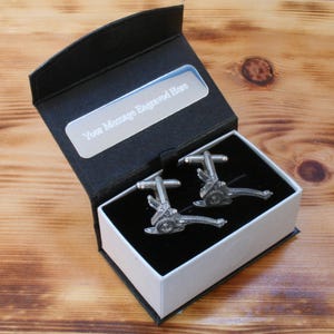 May include: A black gift box with a silver plate that says "Your Message Engraved Here". The box contains two silver cufflinks in the shape of cannons.