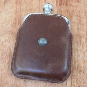 May include: A brown leather flask with a silver top and a silver button on the front.