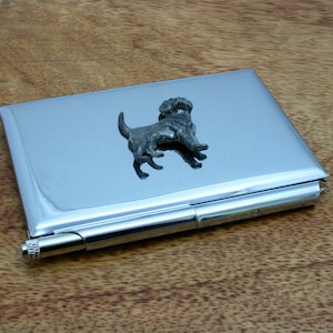 May include: A silver metal card holder with a black dog figurine on the front. The card holder has a hinged lid and a small metal loop on the side.