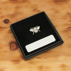 May include: A silver bee pin in a black velvet gift box with a silver plaque for engraving.