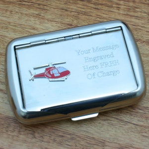 May include: A silver cigarette case with a red helicopter design. The case has a hinged lid and a message engraved on the front: "Your Message Engraved Here FREE Of Charge".