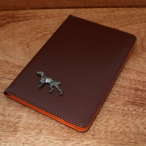 May include: A brown leather notebook with an orange edge and a silver dog figurine on the front.