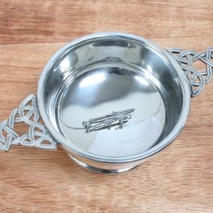 Könnte beinhalten: Eine silberne Schale mit Henkeln im keltischen Knotendesign und glänzender Oberfläche. Die Schale ist leer und hat einen kleinen keltischen Knoten am Boden.