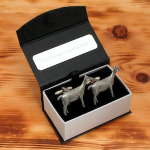 May include: A pair of silver cufflinks in the shape of llamas, presented in a black and white gift box. The box has a white label with the text "Your Message Engraved Here".