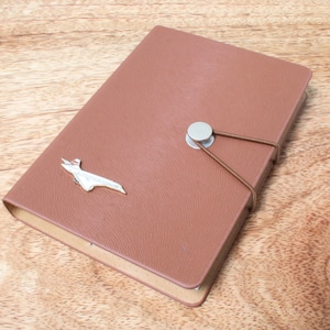 May include: A brown leather-bound journal with a silver airplane charm and a brown elastic closure.