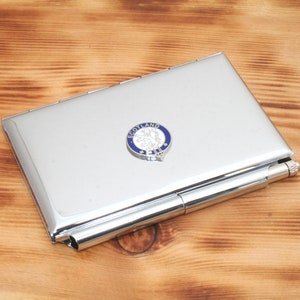 Puede incluir: Un porta tarjetas de metal plateado con un bolígrafo adjunto. El porta tarjetas tiene un escudo escocés de esmalte azul y blanco con el texto "Scotland" en él.