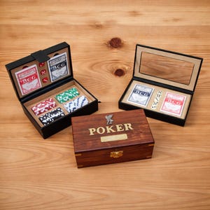 Puede incluir: Tres juegos de póquer exhibidos sobre una superficie de madera. Dos juegos están en cajas negras con naipes, dados y fichas de póquer. También hay una caja de madera con "POKER" grabado.
