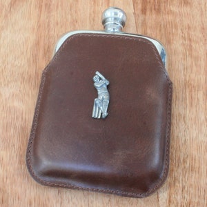 Könnte beinhalten: Eine braune Lederflasche mit einem silbernen Cricketspieler-Design.