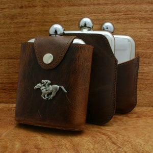 May include: Three silver hip flasks with brown leather cases. The flask on the left has a silver jockey riding a horse design.