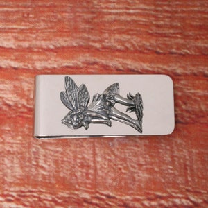 Pode incluir: Clipe de dinheiro de prata com um design detalhado de fada e cogumelo.