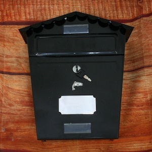 May include: Black metal mailbox with a slot for mail, a keyhole, and a blank nameplate. The mailbox has a decorative scalloped top.