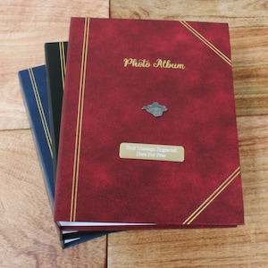 May include: Three photo albums in red, black, and blue. The red album has gold accents, the words "Photo Album" in gold, and a small metal emblem. A gold plaque on the red album reads "Your Message Engraved Here For Free."