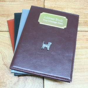 May include: A brown leather address book with a gold metal plate that says "Address Book Your Message Here". A small silver dog figurine is attached to the front cover.