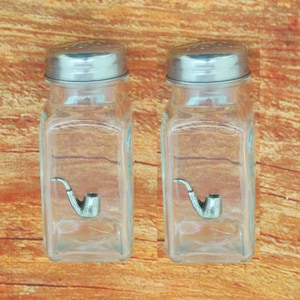 May include: Two clear glass salt and pepper shakers with silver lids and a pewter pipe design on the front.
