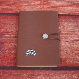May include: A brown leather-bound journal with a chequered flag design and a silver button closure.