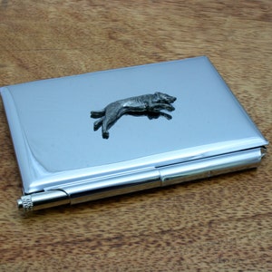 May include: A silver metal card holder with a small silver dog figurine on the front. The dog is running and has a long tail.