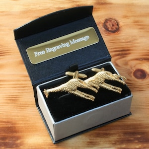 May include: A black gift box with a silver lid, containing a pair of gold giraffe cufflinks. The box has a gold plaque that reads "Free Engraving Message".