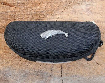 May include: Black zippered case for sunglasses with a silver whale charm on the front.