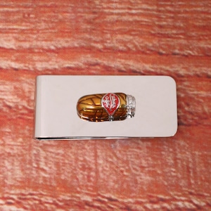 May include: A silver money clip with a red and gold enamel design of a jar of jelly beans. The jar has the words "Jelly Belly" printed on it.