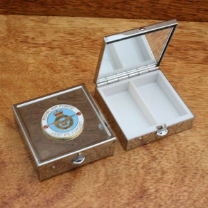 May include: A silver pill box with a mirrored lid and a compartment for pills. The box has a Royal Air Force emblem on the front with the words "Royal Air Force" and "lest we forget".