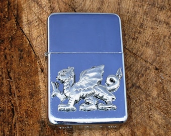 May include: A silver lighter featuring a raised, detailed design of a Welsh dragon on the front.