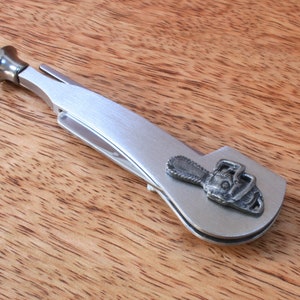 Peut inclure: Un outil en métal argenté pour pipe avec un tamper intégré et un petit motif de tronçonneuse sur le côté.