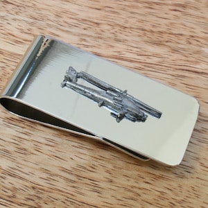 Könnte beinhalten: Silberner Geldclip mit einem detaillierten Design von zwei Kanonen.