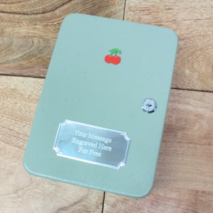 May include: A green metal key box with a cherry design and a silver plaque that says "Your Message Engraved Here For Free".