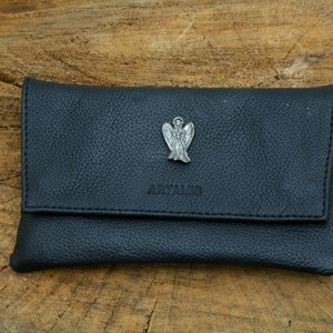 May include: A black leather cigarette case with a silver angel charm and the word "ARTAMIS" embossed on the front.