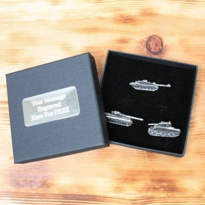 Może przedstawiać: Czarne pudełko prezentowe z srebrną tabliczką z napisem "Your Message Engraved Here For FREE". Pudełko jest otwarte i widać trzy srebrne spinki do mankietów w kształcie czołgu.