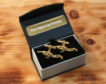 May include: Gold cufflinks in a black and silver gift box. The cufflinks feature a design of two scuba divers. The box has a gold plaque that says "Free Engraving Message".
