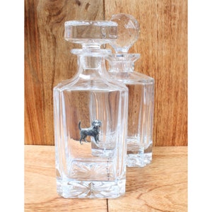 Può includere: Due decanter in vetro trasparente con tappi. Il decanter a sinistra ha una piccola figurina di cane d'argento all'interno. Entrambi i decanter hanno un design testurizzato e sfaccettato.