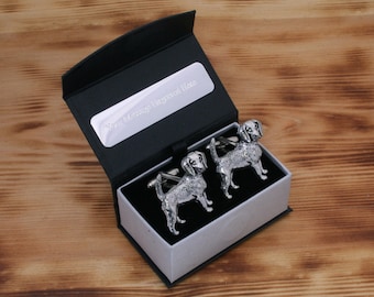 Puede incluir: Un par de gemelos de plata en forma de perro, presentados en una caja de regalo negra con interior blanco. La caja tiene una placa de plata con el texto "Su mensaje grabado aquí".