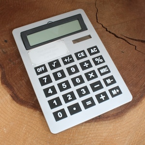 May include: A silver calculator with black buttons and a black display. The calculator has a variety of functions, including addition, subtraction, multiplication, division, square root, percentage, and memory functions. The calculator also has an off button and a clear button.