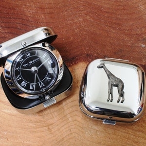 Puede incluir: Dos cajas de metal plateado, una con una esfera de reloj que dice "WM. WIDDOP" y la otra con un diseño de jirafa plateada.