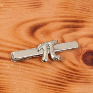 May include: Silver tie clip with a pi symbol design.