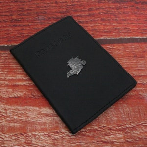 May include: Black passport holder with the word "PASSPORT" embossed on the front. The holder has a small metal emblem of a plane on the front.