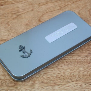 May include: A silver metal tin with a silver anchor charm on the front. The tin has a white label with the text "Remarkable Things" printed on it.