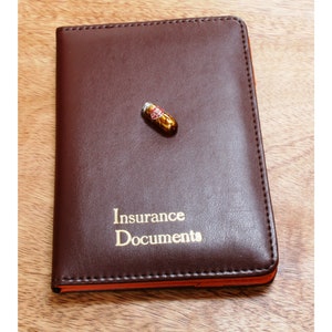 May include: A brown leather insurance document holder with gold lettering that reads "Insurance Documents".
