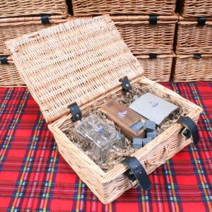 May include: A wicker basket with a lid, filled with brown paper shreds. Inside the basket are a glass bottle, a wooden box, a metal flask, and a set of gray stones.