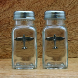 以下が含まれることがあります： 銀色の蓋が付いたガラス製の塩と胡椒の入れ物のセット。それぞれの入れ物には、小さなピューター製の飛行機が入っています。