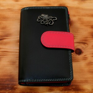 May include: A black leather wallet with a red flap and a silver octopus charm. The wallet has a stitched design around the edges.
