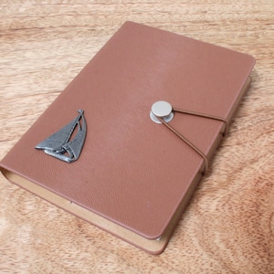 May include: A brown leather journal with a silver sailboat charm and a brown leather strap closure.