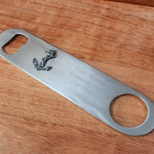 May include: Silver bottle opener with an anchor charm. The opener has a space for a personalized message, "Your Message Engraved Here! For Free 4 Lines".