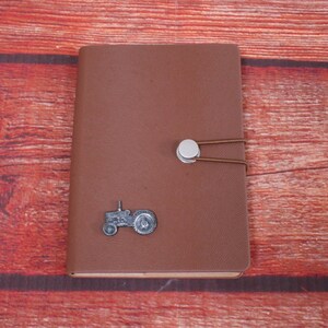 May include: A brown leather-bound journal with a metal tractor design and a silver metal closure.