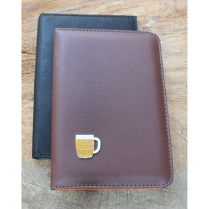 May include: Two leather-bound journals, one brown and one black, with a small beer mug charm on the brown journal.