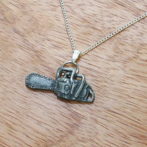Puede incluir: Un collar de cadena de plata con un colgante detallado en forma de motosierra.